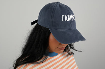 Lady wearing a striped shirt and IAMOR cap holding on a white background