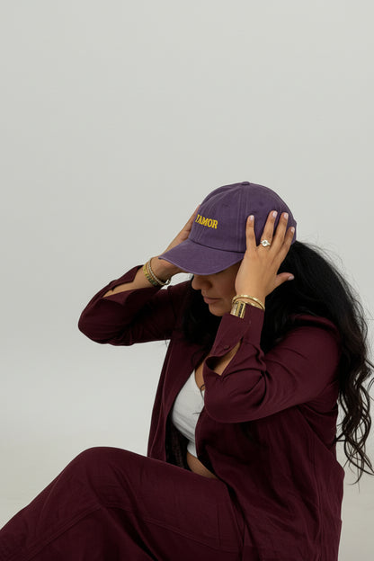 Person wearing a burgundy outfit with various hats and a 'FAMOR' bag on a white floor.